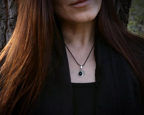 May include: A silver necklace with a black gemstone pendant. The pendant is a round stone with a silver setting. The necklace is worn by a person with long brown hair.