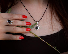 May include: A silver necklace with a black gemstone pendant. The pendant is shaped like a circle with a small design around the edge. The necklace is worn by a person with red nail polish.