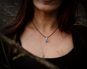 May include: A silver necklace with a blue gemstone pendant. The pendant is set in a silver frame with a delicate design.