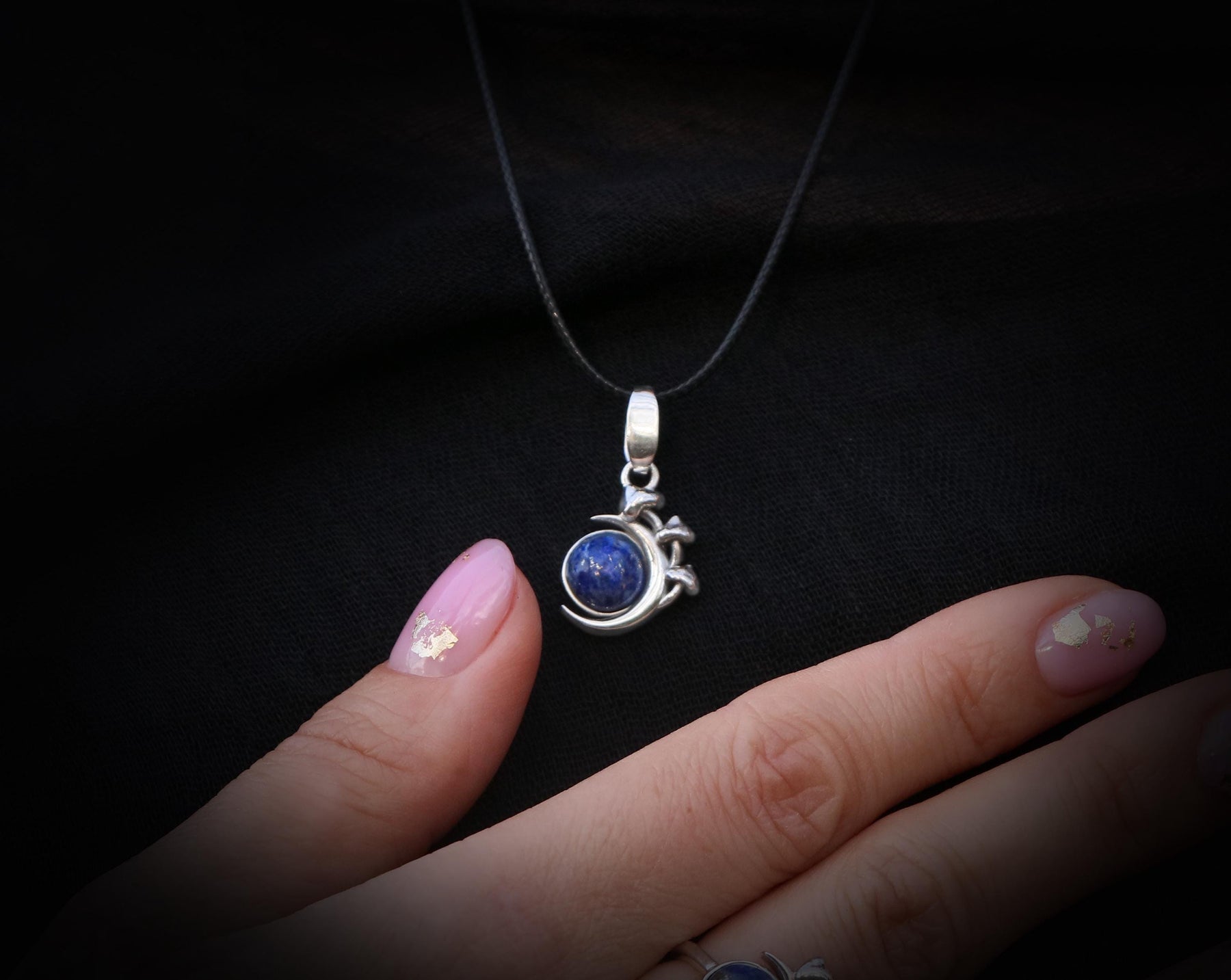 May include: A silver necklace with a blue gemstone pendant. The pendant is shaped like a crescent moon with a small star on each side.