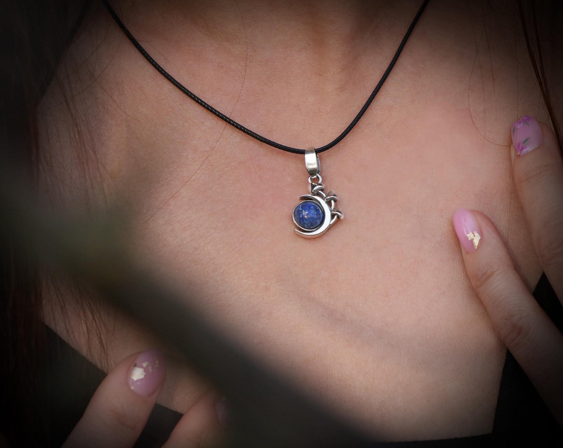 May include: A silver necklace with a blue gemstone pendant. The pendant is shaped like a crescent moon with a small star design.