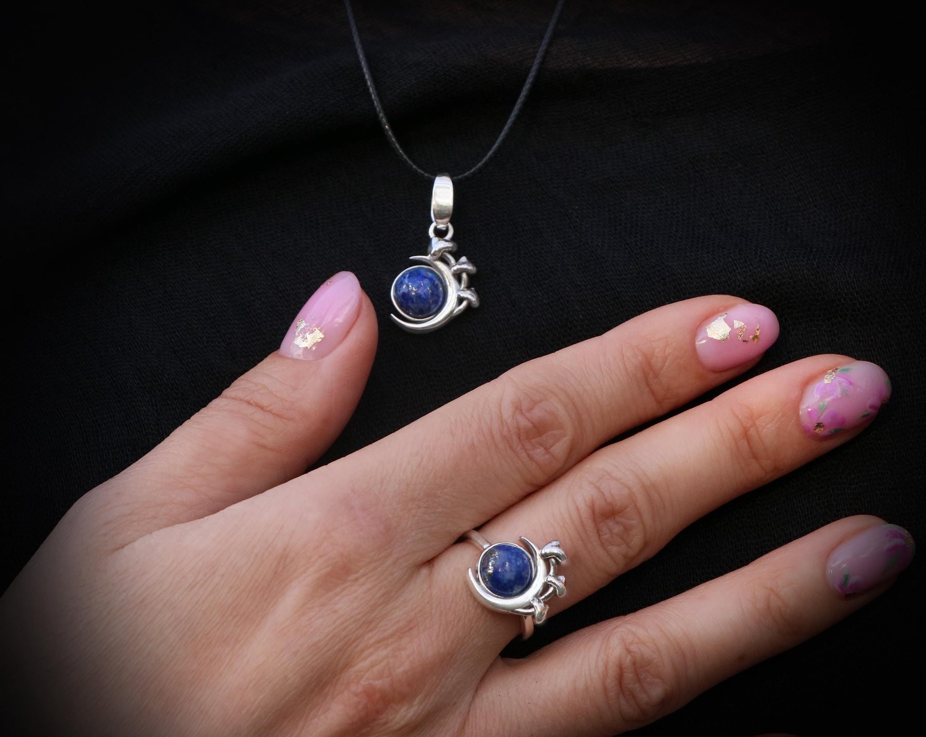May include: A silver necklace and ring with a blue gemstone pendant and ring. The pendant and ring are both in the shape of a crescent moon with a small flower design.